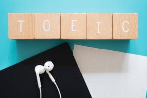 toeic listening; five wooden blocks with toeic text of concept, a black notebook, a piece of paper, and a pair of earphones.