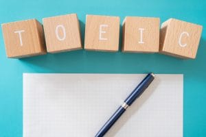 toeic writing; five wooden blocks with toeic text of concept, a piece of paper, and a blue pen.